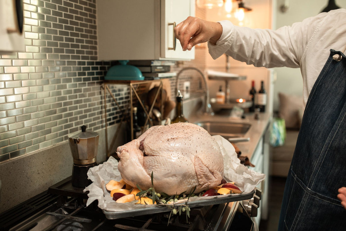 Whole uncooked turkey being seasoned in a roasting pan before Thanksgiving