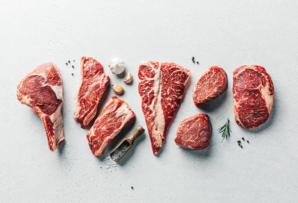 Grass-fed beef cuts: ribeye, strip, T-bone, filet and sirloin laid out on a counter